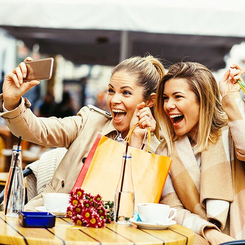 Two smiling women taking selfies while shopping at Miracle Mile Shops