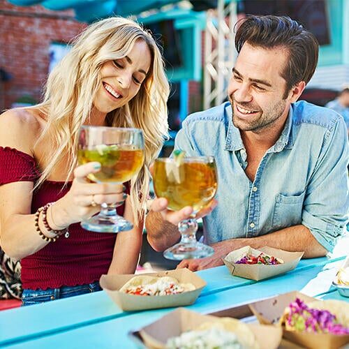 Smiling couple celebrating with drinks while shopping at Miracle Mile Shops